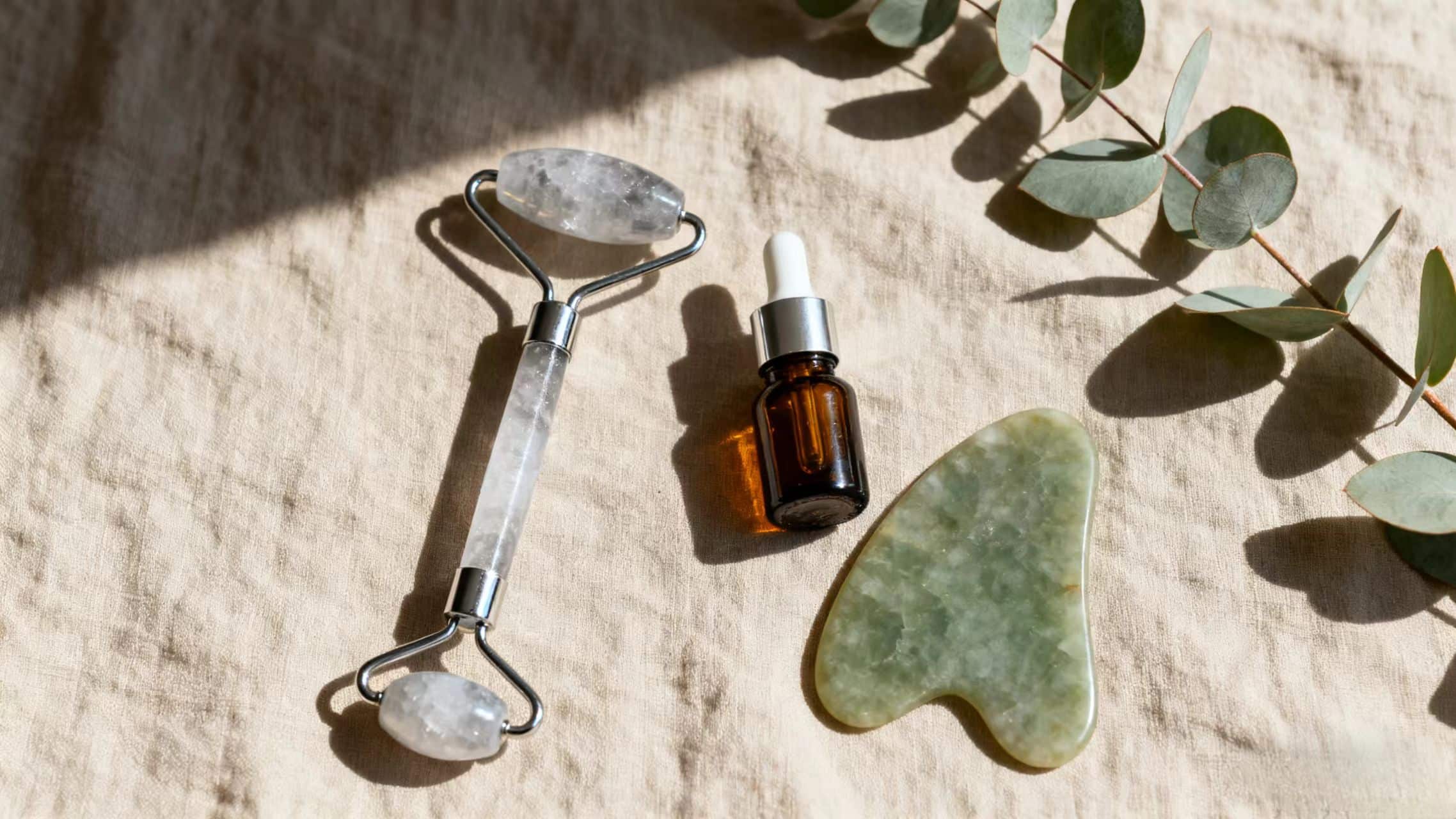 Minimal beauty tools including ice roller and gua sha on beige linen background